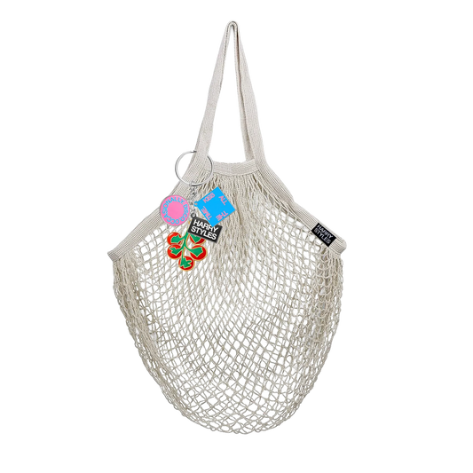 Cream mesh string grocery bag by Harry Styles with a tomato and food charm keychain attached